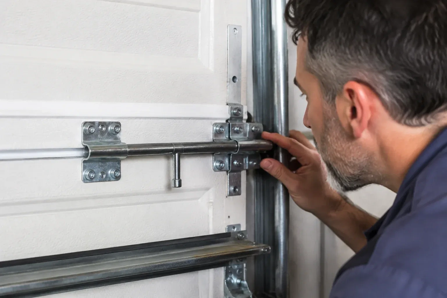 Person leaning close to a white paneled door, one hand on a metal slide-bolt bar mounted across the panel. — Garage Door Manual Lock Repair, Clarington