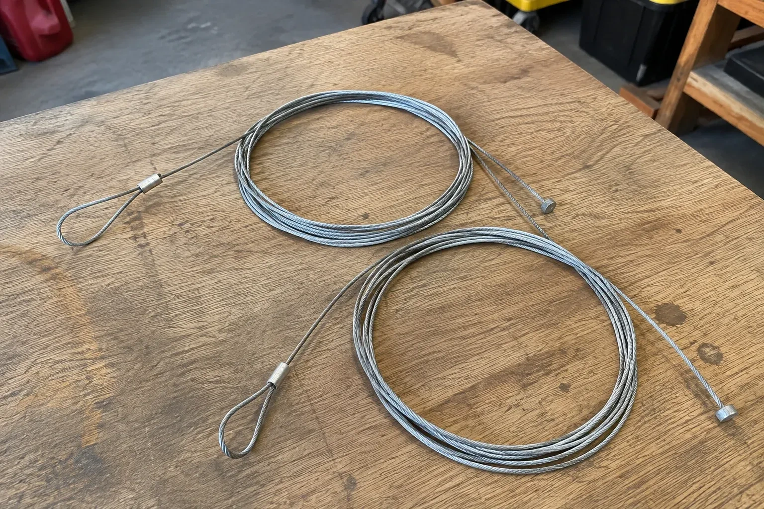 Two coiled steel cables with loop and stop ends on a workbench. — Garage Door Cable Replacement, Clarington